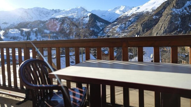 Een balkon met een tafel en stoel, met uitzicht op besneeuwde bergen.