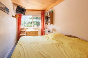 Ein Schlafzimmer mit einem Bett, einem Schreibtisch, einem Stuhl, einem Fernseher und einem Fenster mit Vorhängen.