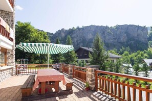 Ein Balkon mit Tisch und Stühlen, einem gestreiften Sonnenschirm und Blick auf einen Berg und Bäume.