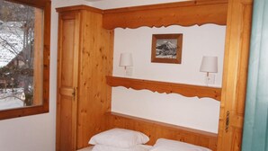A bedroom with a wooden headboard, two bedside lamps, a framed picture, and a window with a view of trees and snow. - 300m from ski slopes, 2nd floor, swimming pool, balcony, tv, 45m², Valloire (Valloire)