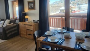 A dining area with a table set for four, a sofa, and a wooden cabinet. - 15m from ski slopes, 2nd floor, view ski slopes, balcony, tv, ski locker, 55m², Valmorel (Valmorel)