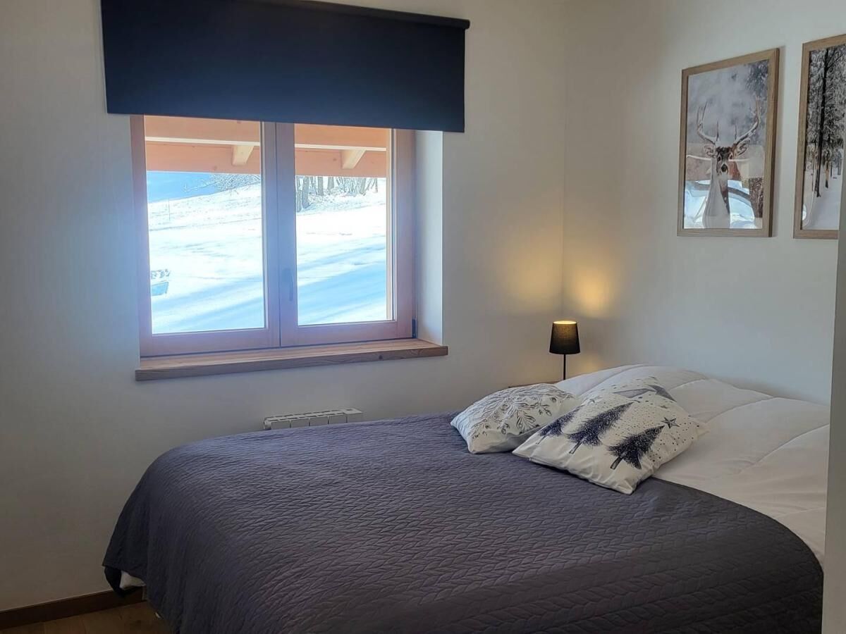 Un dormitorio con una cama, una ventana que ofrece vistas a un paisaje nevado y dos cuadros colgados en la pared.