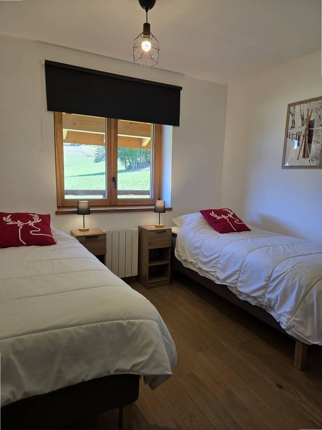 Een slaapkamer met twee bedden, een raam met uitzicht op groen, een aan de muur hangend schilderij en een geometrische hanglamp.