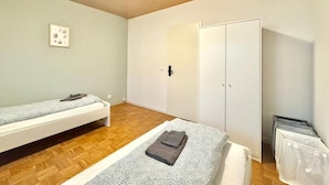 A small, well-lit room with two single beds, a wardrobe, and a trash bin. - Family Apartments Near City Centre (Frankfurt)