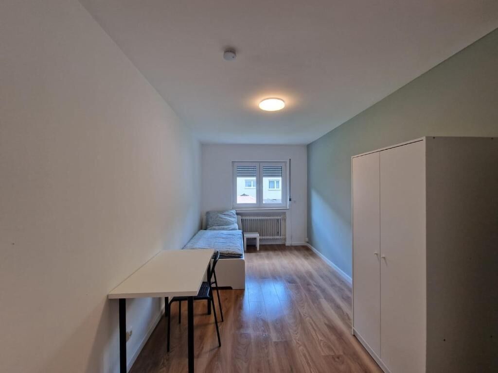 Una habitación pequeña con una cama, una mesita y un armario.