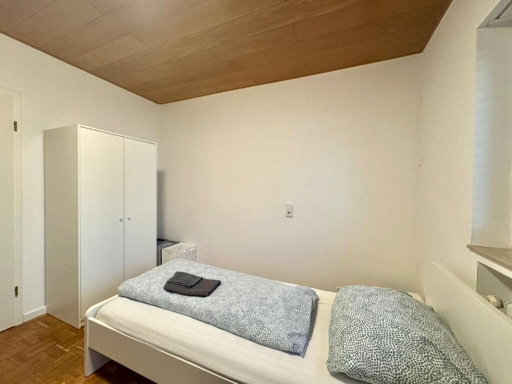 Een kleine kamer met een enkel bed, houten plafond, een kast en een klein nachtkastje.