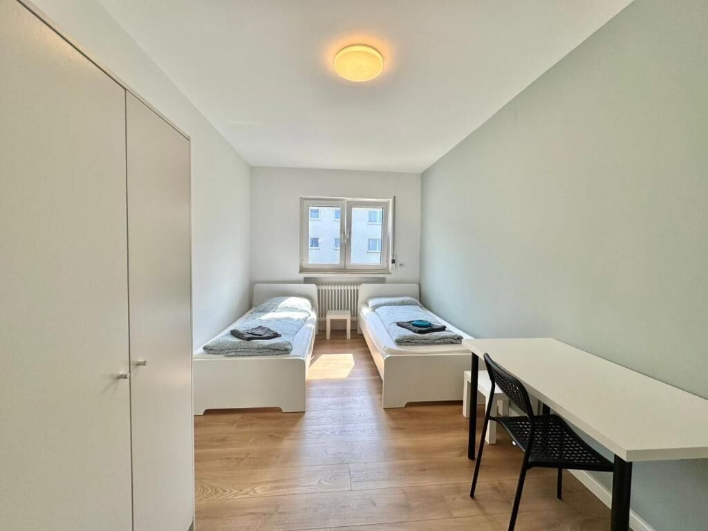 A small, bright room with two single beds, a white table, and a radiator.