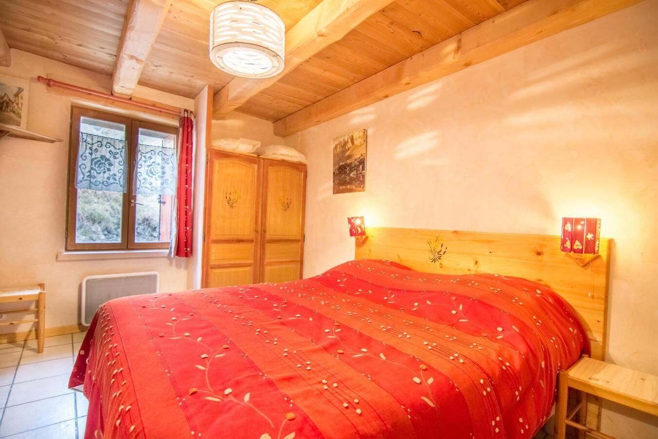 Une chambre confortable avec une tête de lit en bois, une couvre-lit rouge, une fenêtre avec des rideaux et un radiateur.