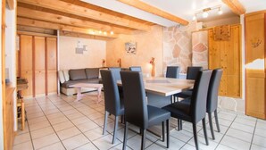 A dining area with a wooden table and chairs, a sofa, and a stone wall. - 1st floor, terrace, tv, ski locker, 85m², Valloire (Valloire)