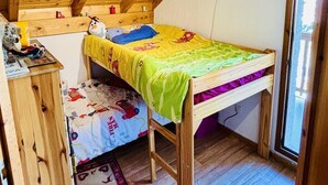 Ein gemütliches Schlafzimmer im Dachgeschoss mit Holzbalkendecke, einem Etagenbett, einem kleinen Schreibtisch und einem Fenster.