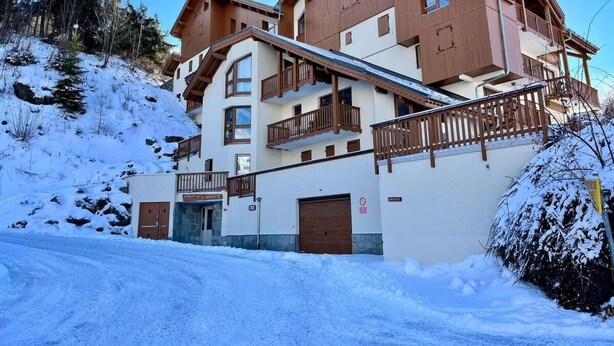Ein mehrstöckiges Hotel mit Holzfassade, Balkonen und verschneiter Landschaft.