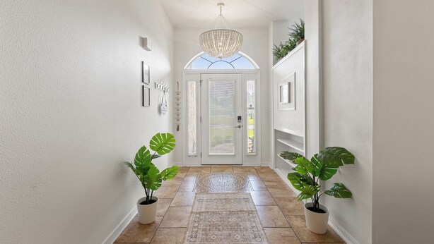 A hallway with a white door, potted plants, a patterned rug, and a chandelier. - Spacious, Family-Friendly 5 Bedroom Home with Salt Water Pool (Navarre)