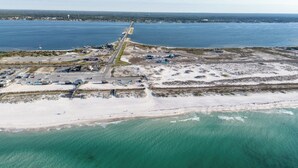Vista aerea di una zona costiera con una strada che conduce a una spiaggia, acque cristalline turchesi e vegetazione rada.