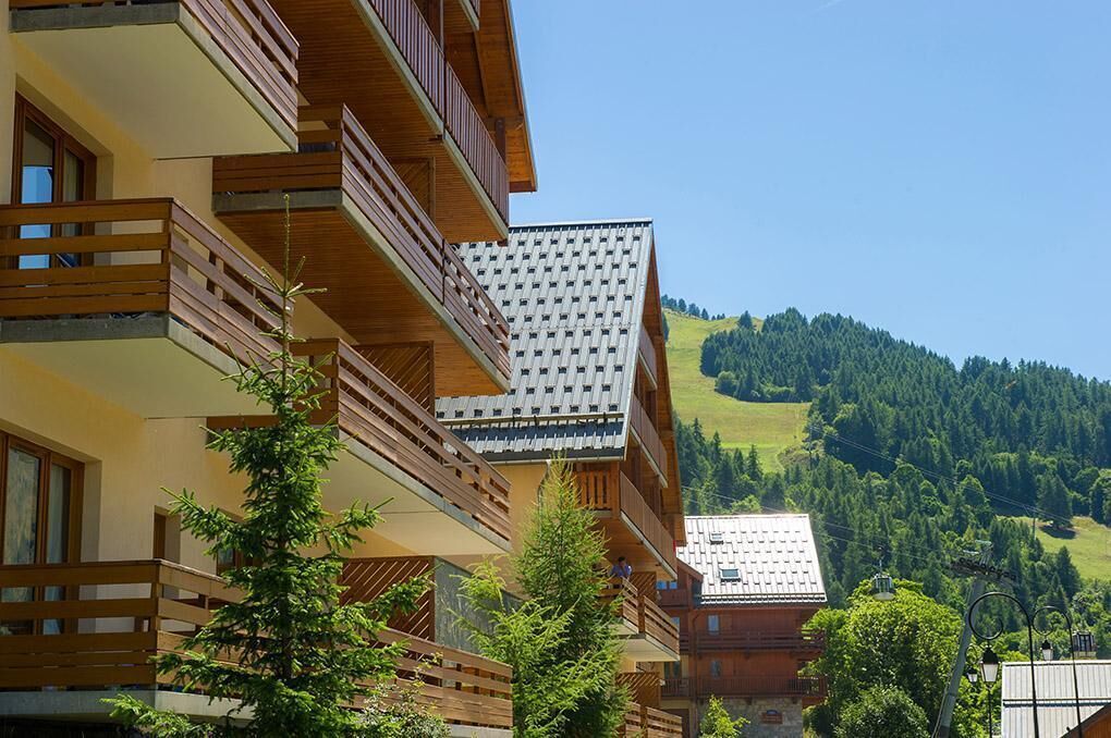 A multi-story building with wooden balconies and a view of a green hillside.