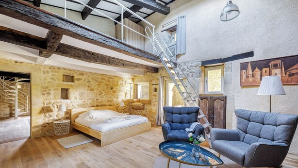 A spacious room with a wooden floor, a bed, a blue armchair, and a round coffee table. A staircase leads to an upper level. - 2-bedroom with pool near Saint Emilion (Guillac)