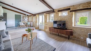 A spacious living area with a wooden TV stand, a dining table with chairs, and a large window with a view of greenery. - 2-bedroom with pool near Saint Emilion (Guillac)