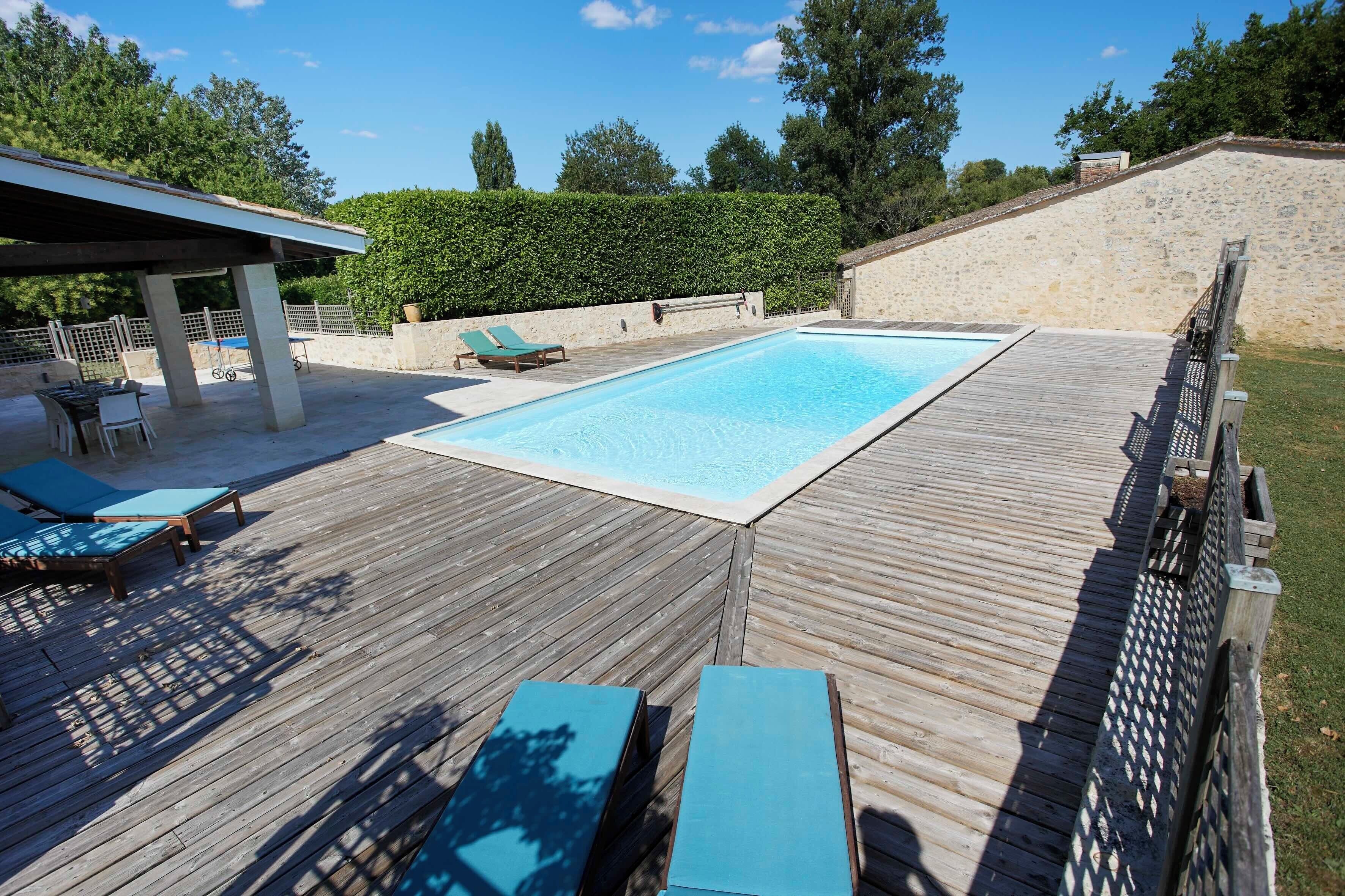 A wooden deck with a swimming pool, lounge chairs, and a covered seating area.