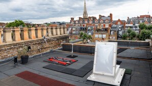 Eine Dachterrasse mit Blick auf einen historischen Kirchturm, Backsteingebäude und eine moderne Struktur im Hintergrund.