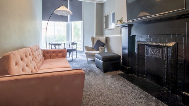 A living room with a tufted sofa, a black fireplace, a dining table with chairs, and a pendant light. - Pass the Keys | Cosy in Fabulous West End (Glasgow)