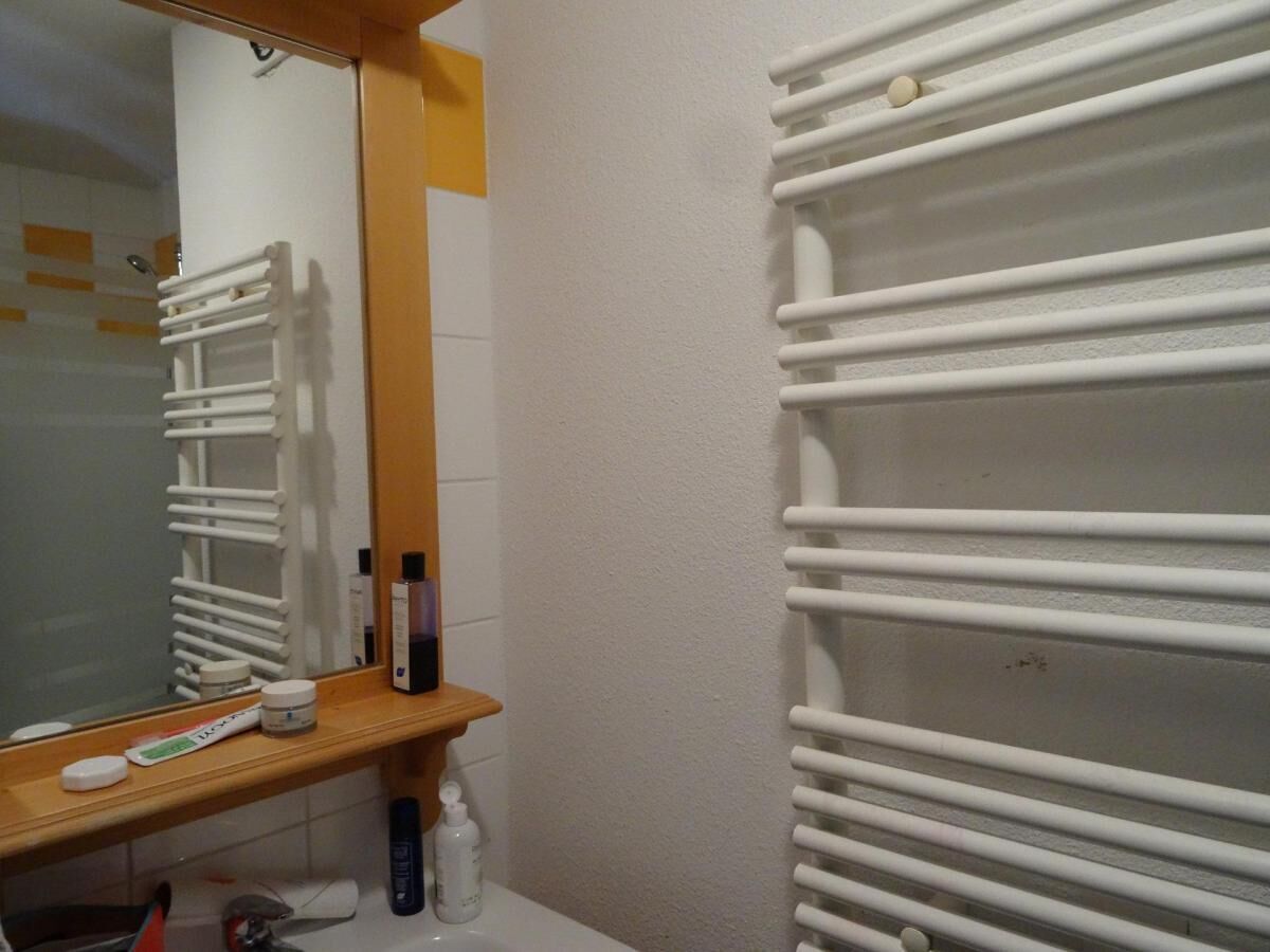 Un baño con una bañera blanca, un estante de madera con artículos de aseo y un espejo.