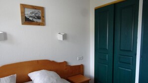 A bedroom with a wooden headboard, two white pillows, a bedside table, a framed picture on the wall, and a teal double door. - 300m from ski slopes, 3rd floor, swimming pool, balcony, tv, 46m², Valloire (Valloire)