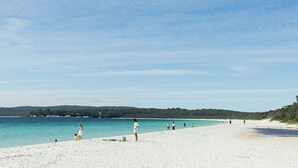 A beach with white sand, clear turquoise water, and a distant forested hill.