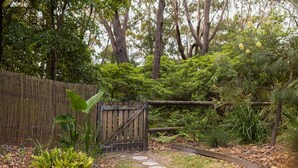 A wooden gate in a lush garden with dense foliage and trees in the background.