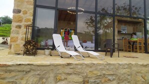Een modern gebouw met een gevel van natuursteen, grote glasramen en een patio met twee witte lounge fauteuils.