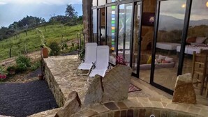 Een stenen jacuzzi met glazen omheining, witte lounge stoelen en uitzicht op een bergachtig landschap.