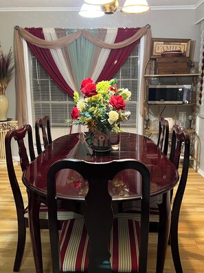 Uma sala de jantar com uma mesa redonda rodeada por cadeiras, um vaso de flores e uma estante com um letreiro escrito 'FAMILY'.