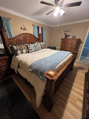 Quarto com cama de madeira, mesa de cabeceira, penteadeira e ventilador de teto.