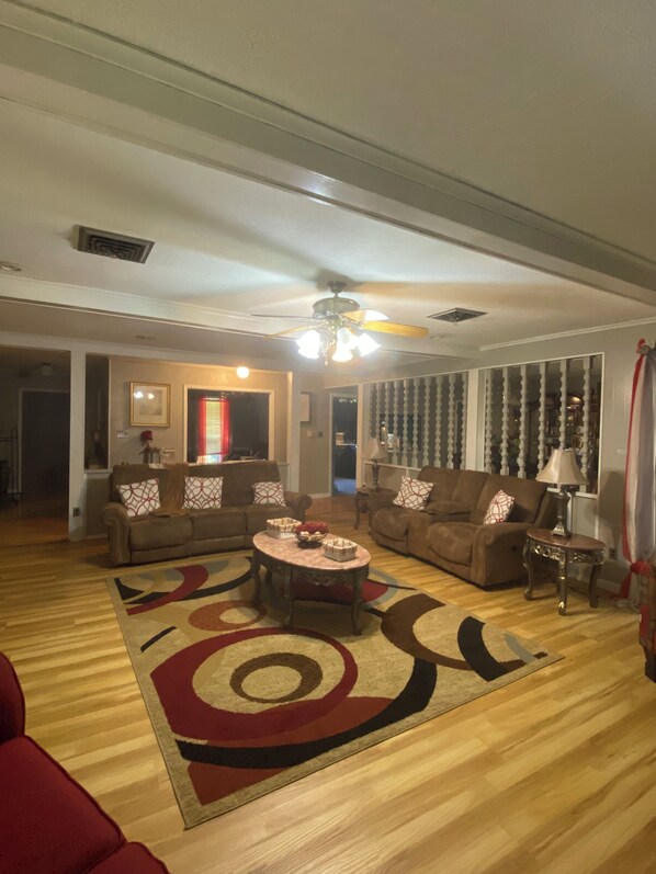 Uma sala de estar com ventilador de teto, dois sofás, uma mesa de centro e um tapete estampado.