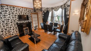 A living room with a fireplace, leather sofas, a TV, and a dining area with chairs and a table. - Roomy home 1 level Free Parking (Edinburgh)
