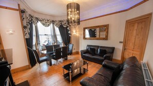 A living room with a black leather sofa, a glass coffee table, a dining area with a table and chairs, and a chandelier. - Roomy home 1 level Free Parking (Edinburgh)