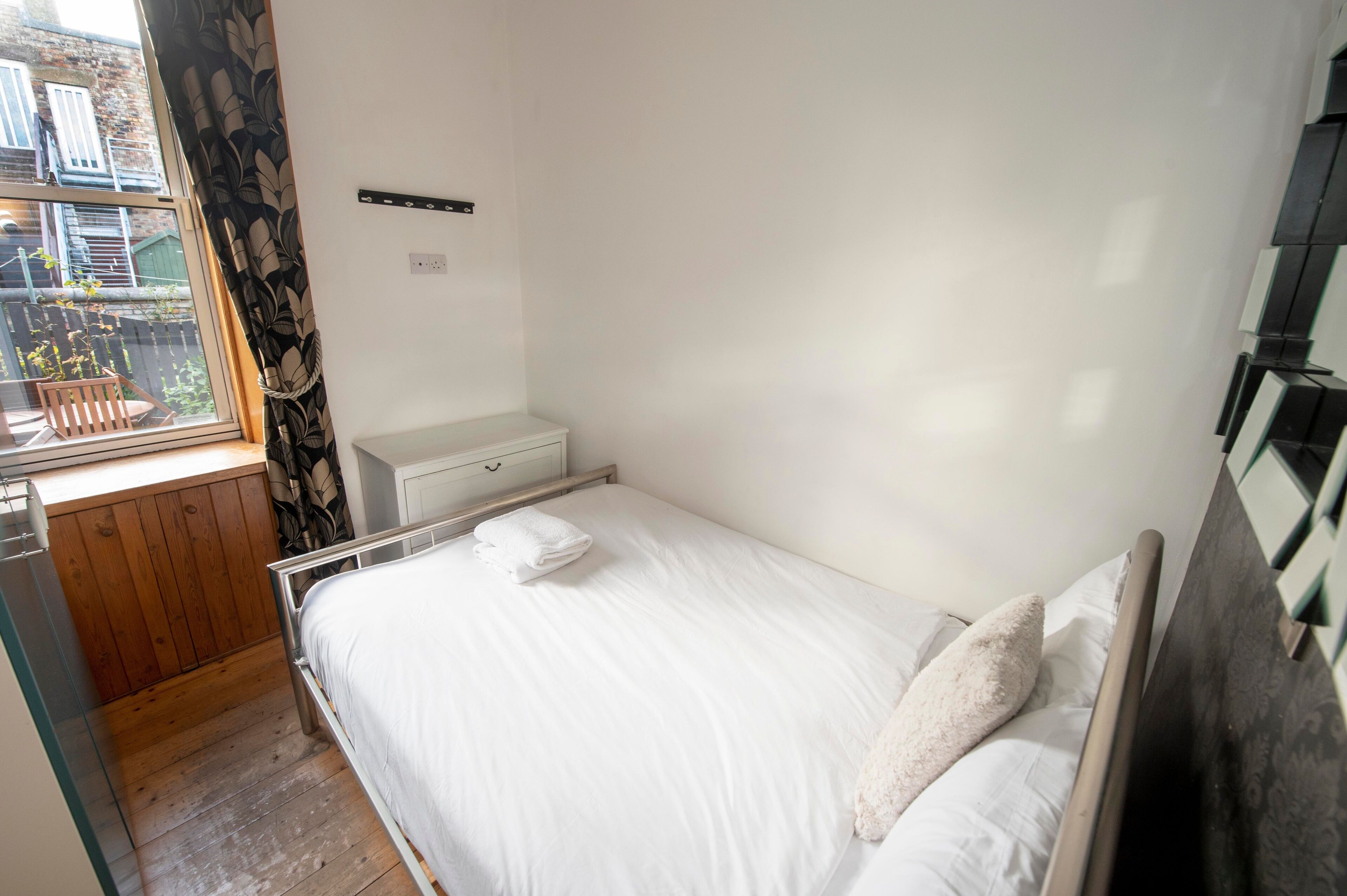 A small, tidy bedroom with a single bed, a bedside table, and a window with curtains.