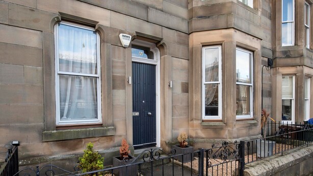A corner building with a dark blue door, a sign above the door, and a small potted plant in front. - Roomy home 1 level Free Parking (Edinburgh)