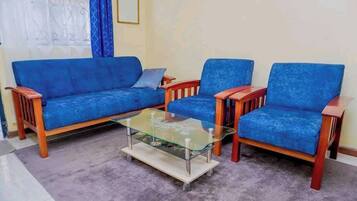 Un salon avec un canapé bleu, deux fauteuils assortis et une table basse en verre.