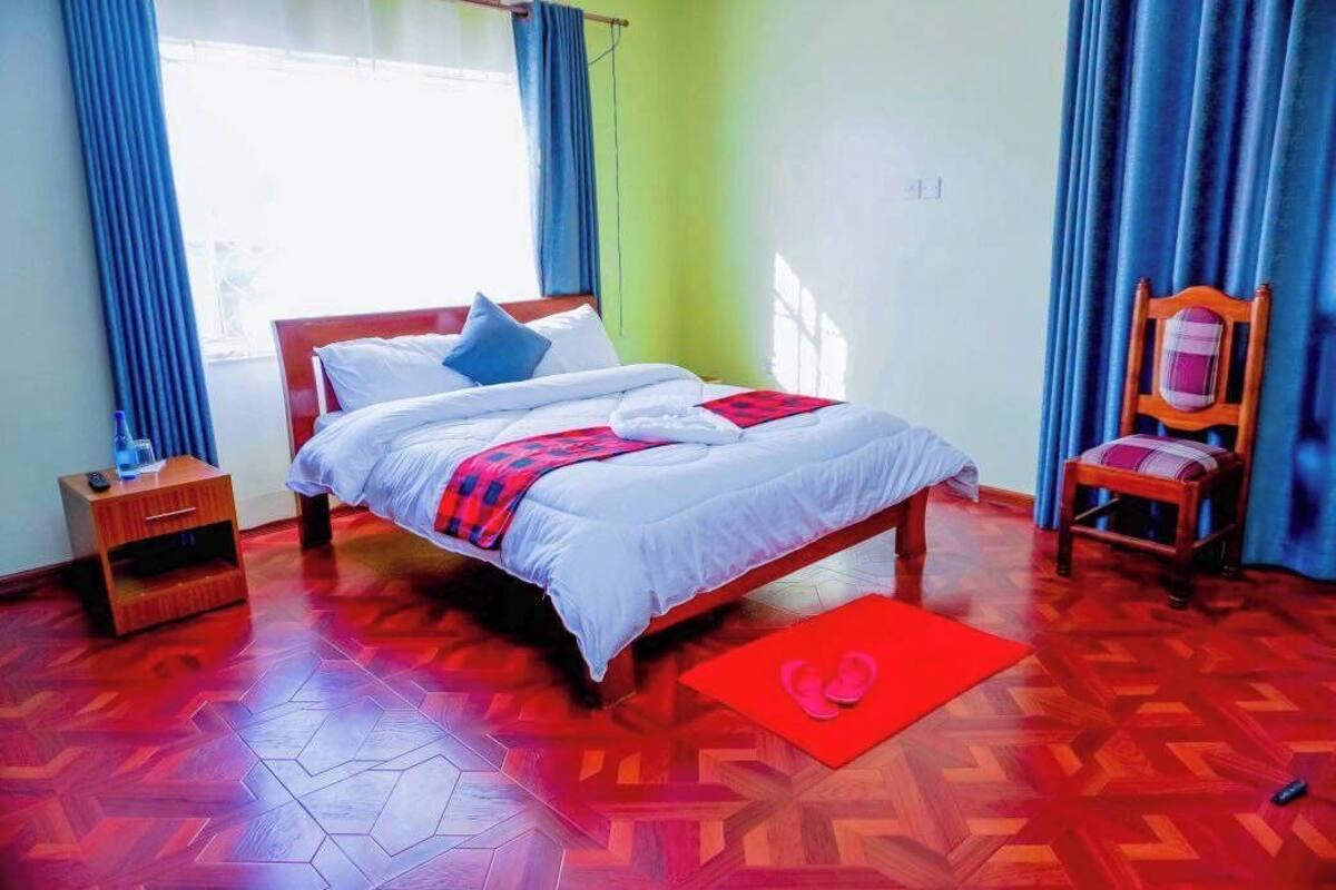 A bedroom with a bed, a nightstand, a chair, and a red mat.