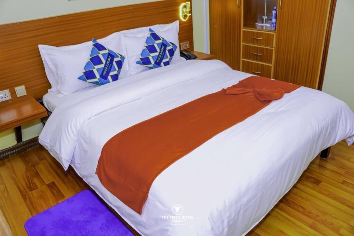 A hotel room with a wooden headboard, a bed with white bedding and a brown throw, a purple bench, and a wardrobe with a mirror.