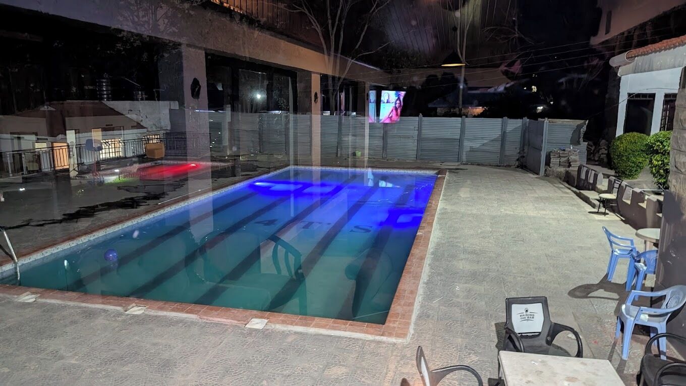 Una piscina exterior con un borde de baldosas, algunas tumbonas y una pantalla de televisión montada en la pared.