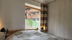 A bedroom with a large bed, a window with a view of a building, and a curtain. - 15m from ski slopes, 1st floor, view ski slopes, balcony, tv, ski locker, 47m², Valmorel (Valmorel)
