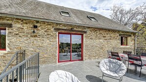 A stone building with a red-framed glass door, outdoor seating with white cushioned chairs, and a tiled patio area. - Authentic Cottage in Peaceful Setting with Private Terrace, Garden, and Wi-Fi (Beynat)