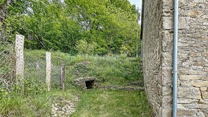 A stone building with a stone wall, a metal pipe, and a small stone structure in the background. - Authentic Cottage in Peaceful Setting with Private Terrace, Garden, and Wi-Fi (Beynat)