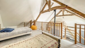A high-ceilinged attic bedroom with a bed, a bean bag, and a staircase. - Authentic Cottage in Peaceful Setting with Private Terrace, Garden, and Wi-Fi (Beynat)