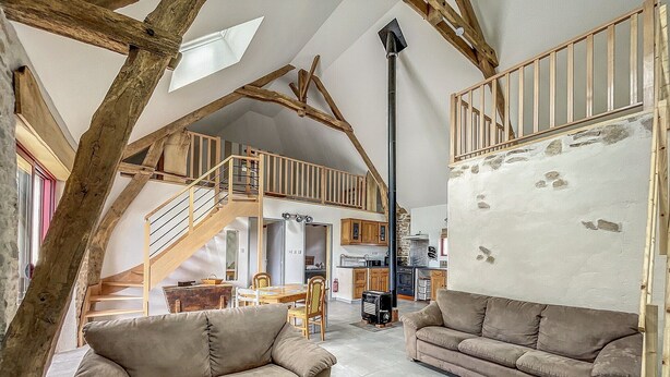 A spacious loft with high ceilings, exposed wooden beams, a central staircase, and a cozy seating area with two sofas. - Authentic Cottage in Peaceful Setting with Private Terrace, Garden, and Wi-Fi (Beynat)
