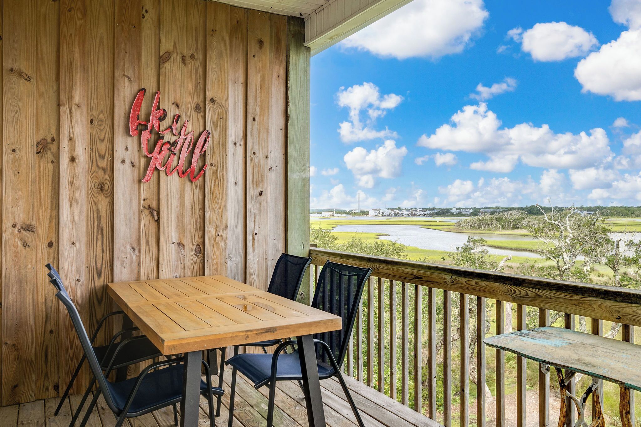 A wooden deck with a table and chairs, a 'Like it' sign, and a view of a golf course.
