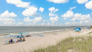 A beach with umbrellas, chairs, and a pier in the background.