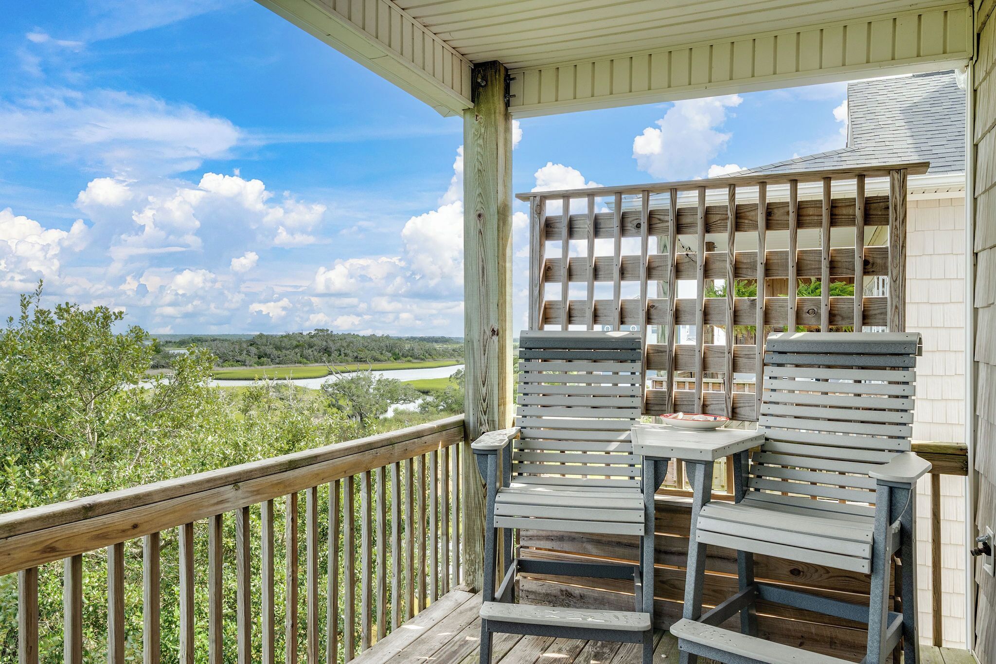 En träveranda med två stolar och ett bord, med utsikt över en flod och grönområden.