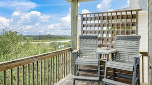 A wooden deck with two chairs and a table, overlooking a river and greenery.