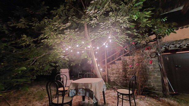 Ein Sitzbereich im Freien mit Tisch und Stühlen, umgeben von Bäumen und einer Steinmauer.